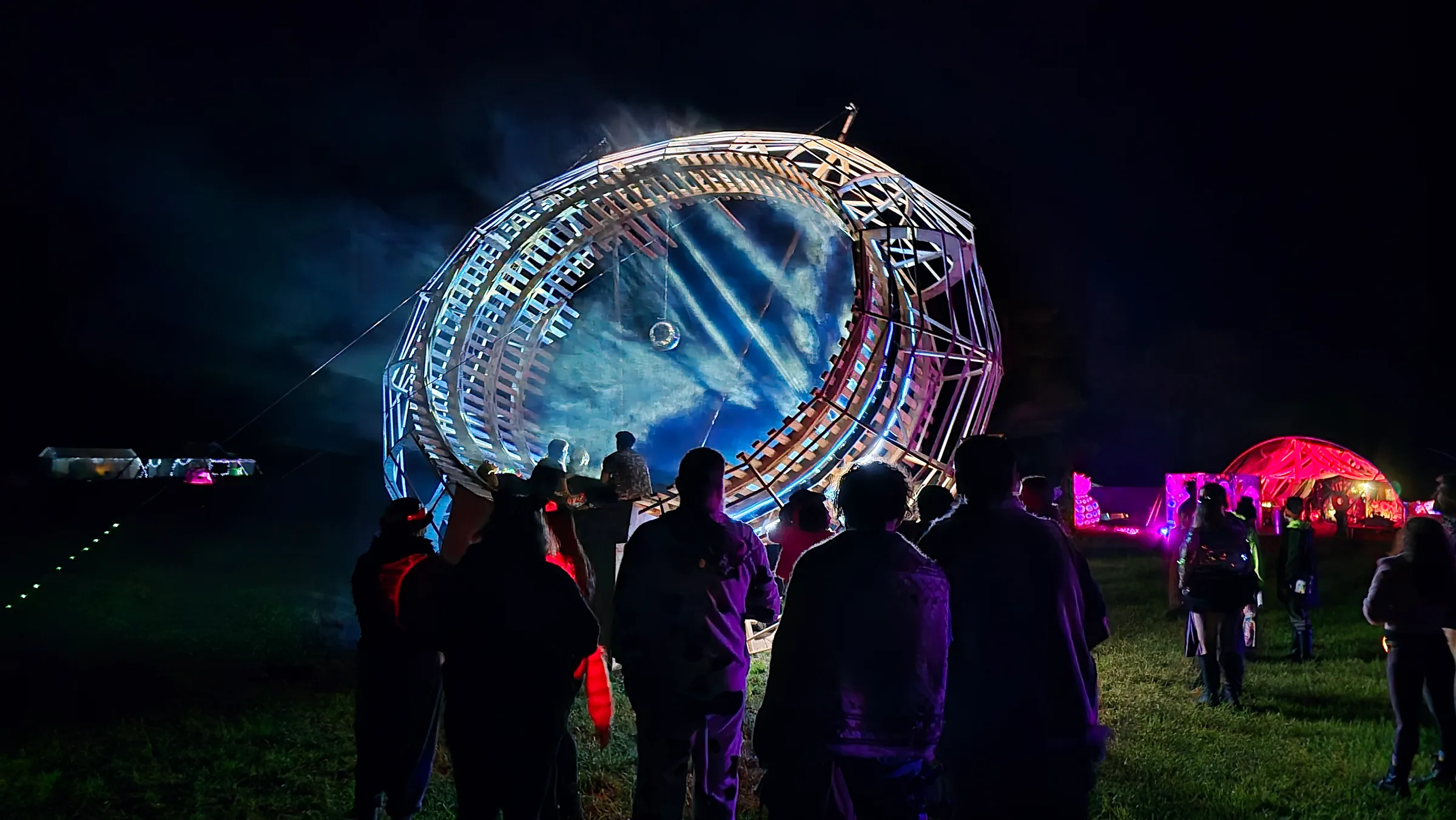Space Donut installation at night: a 25-foot ring projecting generative visuals onto mist above a crowd